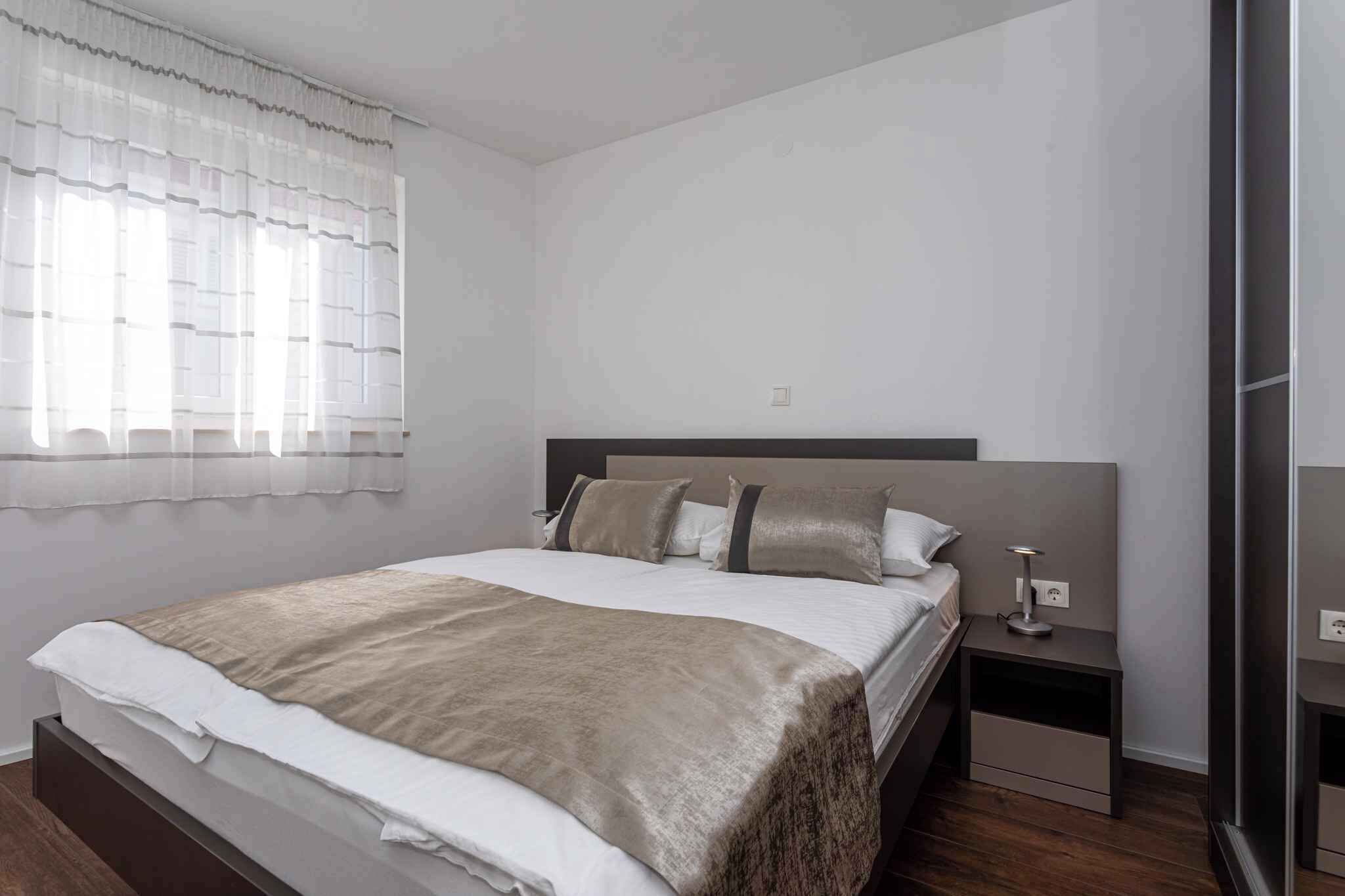 Une chambre moderne avec un grand lit, une table de chevet et une fenêtre ornée de rideaux légers.