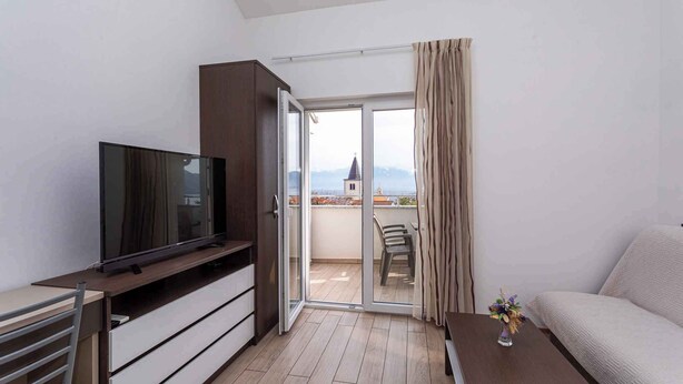 A modern living room with a flat-screen TV, a sofa, a coffee table, and a balcony with a view of a distant building. - Holiday apartment with a balcony and sea view (Baška)