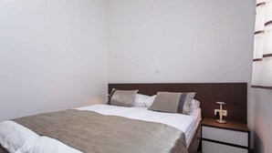 A neatly made bed with a grey blanket and pillows, a bedside table with a lamp, and a wooden floor. - Holiday apartment with a balcony and sea view (Baška)