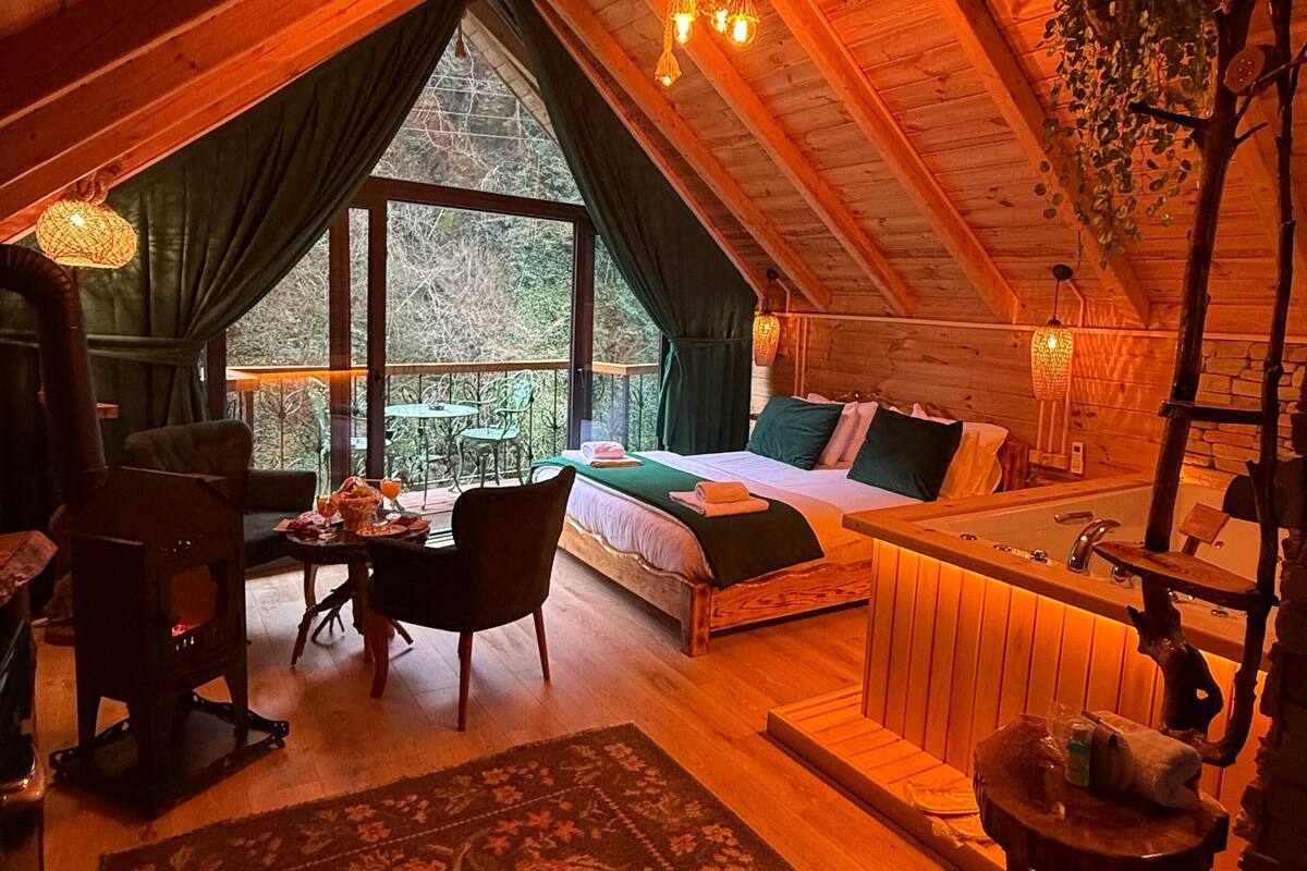 Un dormitorio acogedor en el ático con un ventanal grande, una cama, una mesita y una chimenea.