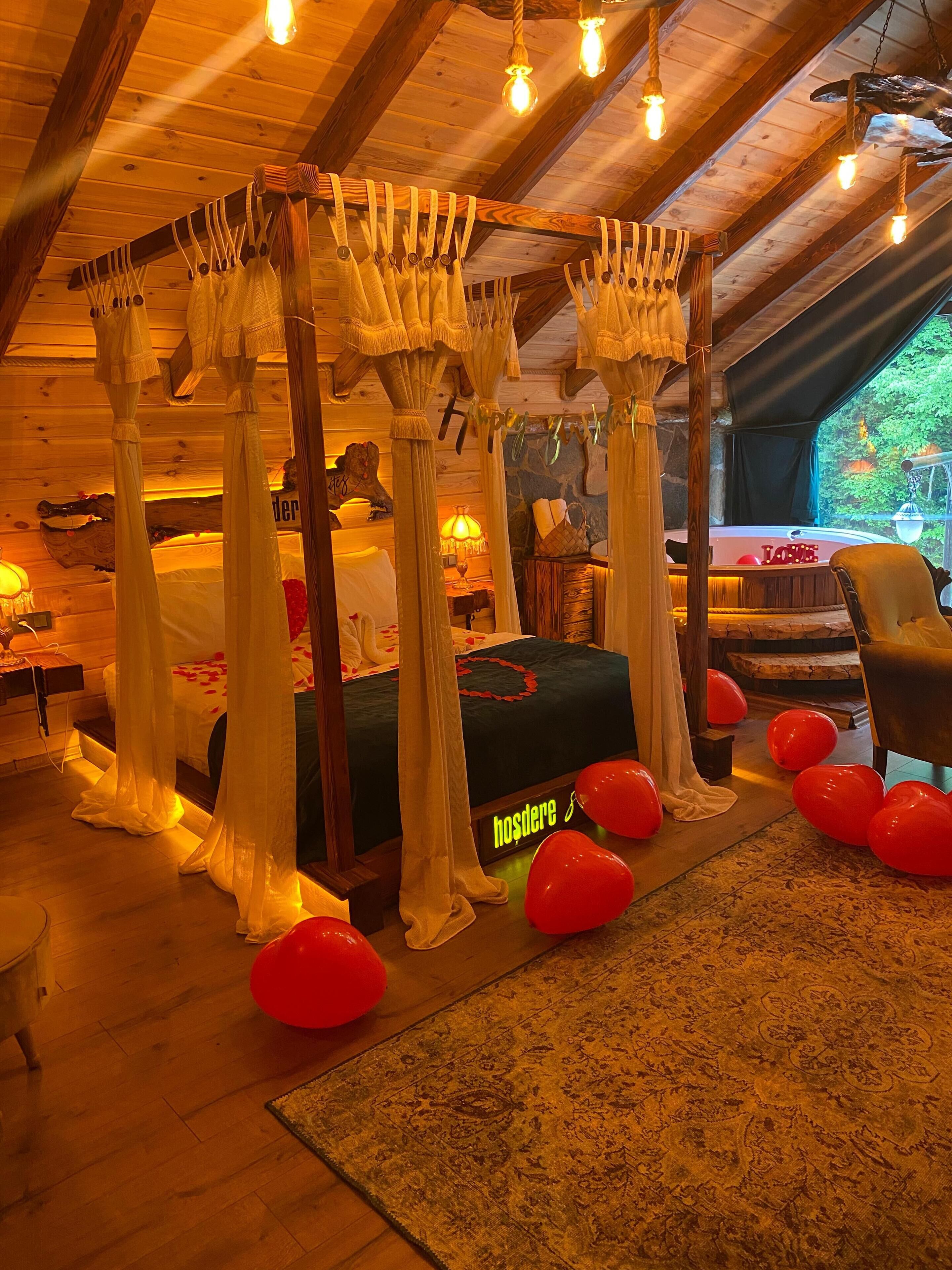 A cozy bedroom with a canopy bed, a bedside table, a lamp, and a view of the outdoors.