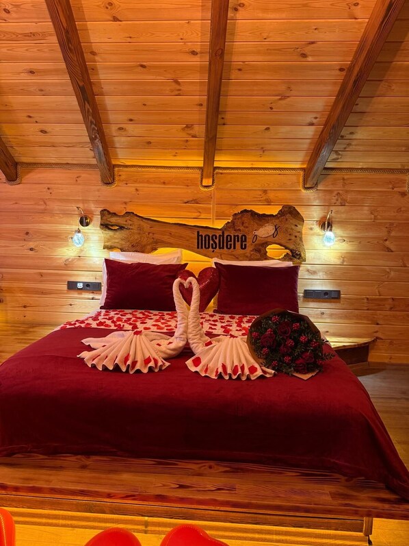 Un dormitorio de cabaña de madera con una cama, ropa de cama roja, toallas con forma de corazón y un ramo de flores.