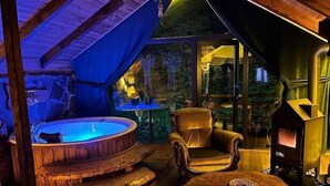 Interior acogedor de una cabaña con un jacuzzi, un sillón cómodo, una mesa de madera rústica y una chimenea.