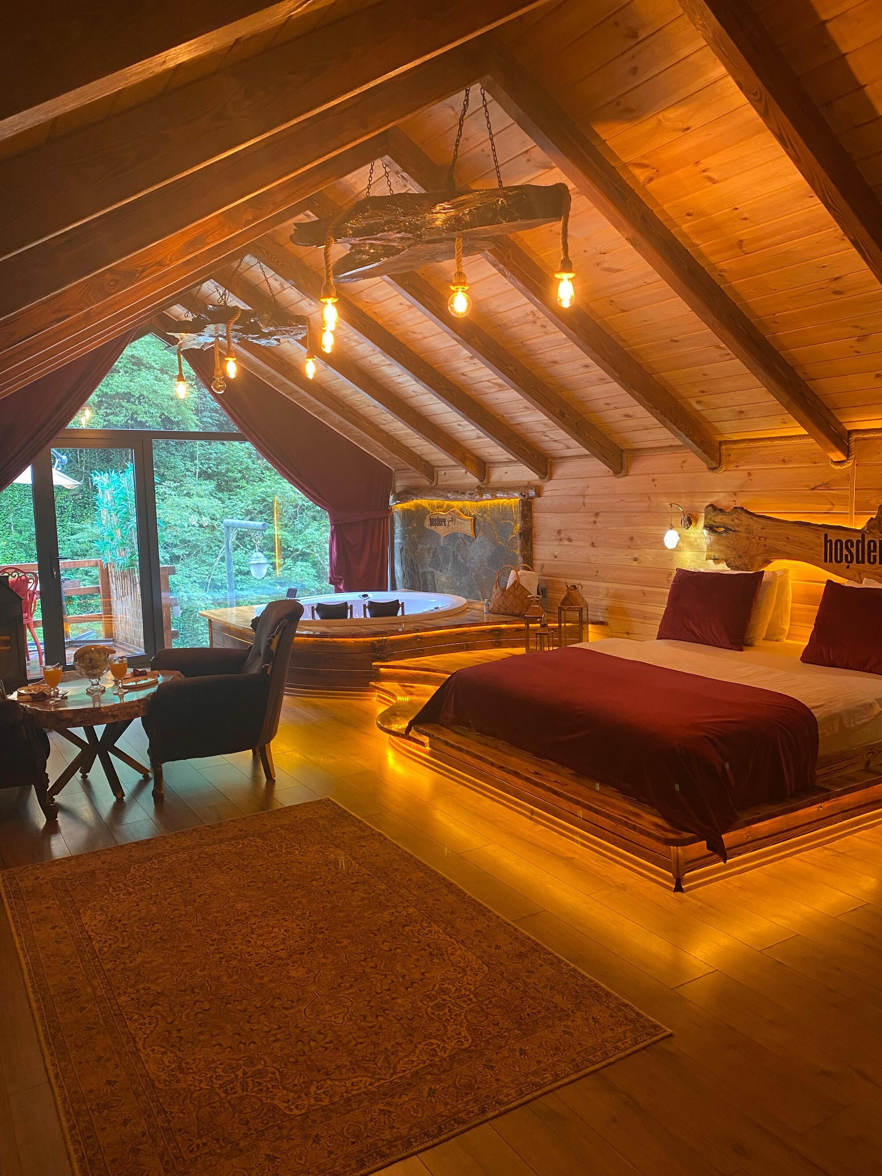 A cozy attic bedroom with a large bed, a sitting area with a table and chairs, and a view of the outdoors.
