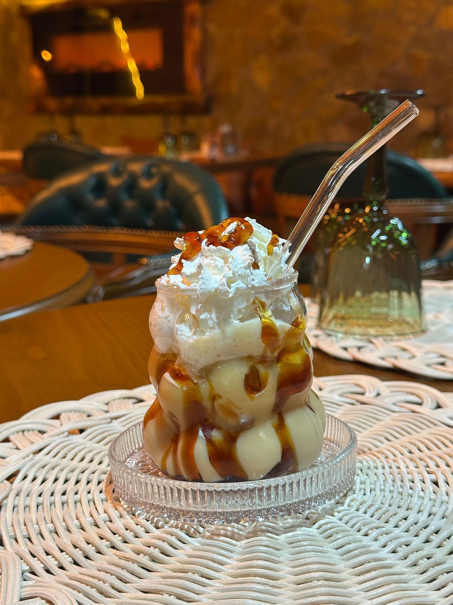 Postre con crema batida y jarabe sobre un plato de vidrio, sobre un mantel tejido.