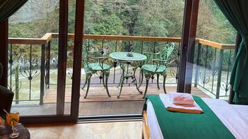 A cozy room with a large window, a wooden ceiling, a green bed, and a table with chairs.
