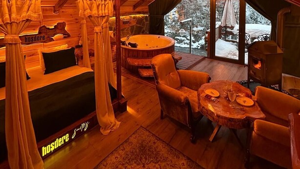 Interior acogedor de una cabaña con techo de madera, una bañera de hidromasaje y un comedor con vistas a un paisaje nevado.