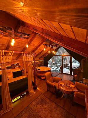 Interior acogedor de una cabaña con techo de madera, una bañera de hidromasaje y un comedor con vistas a un paisaje nevado.