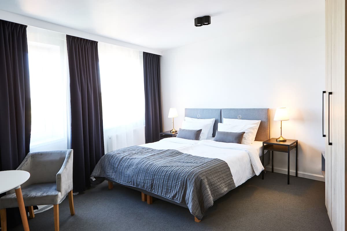 A hotel room with a bed, bedside tables, a chair, and a desk.