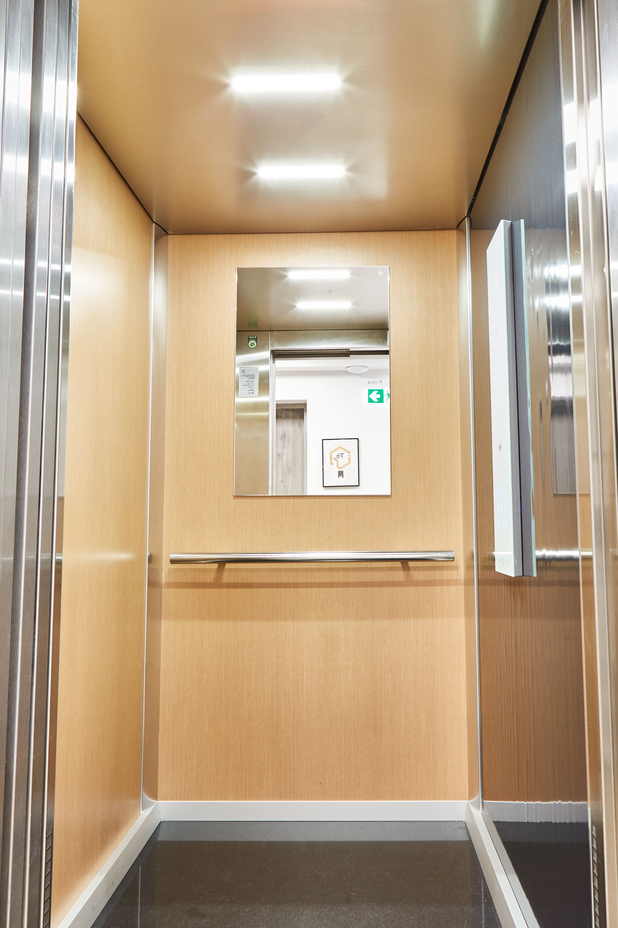 Interior moderno de ascensor con detalles de madera, barandilla y pantalla digital.