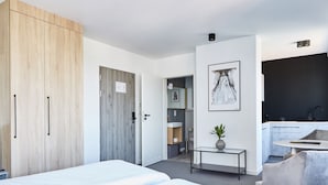 A modern hotel room with a bed, a desk, a chair, a wardrobe, and a kitchenette. - Silesia Apartments (Katowice)