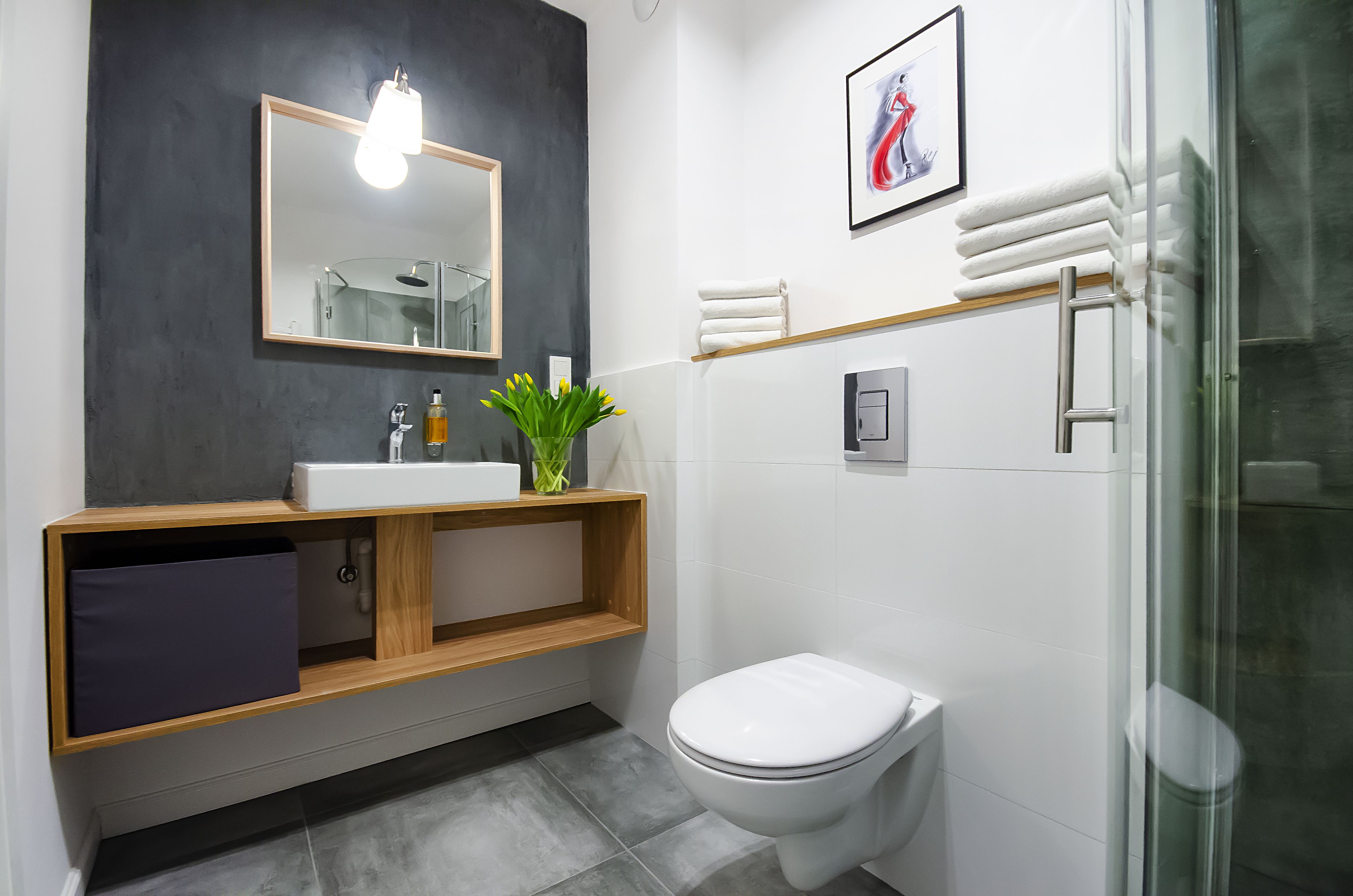 A modern bathroom with a white toilet, a wooden vanity with a sink, a mirror, and a shower area.