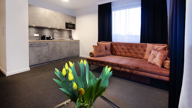 A modern living room with a sofa and a coffee table, a kitchen area with a microwave and sink, and a large window with curtains. - Silesia Apartments (Katowice)