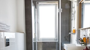 Un baño moderno con cabina de ducha de vidrio, inodoro blanco y tocador de madera con espejo.