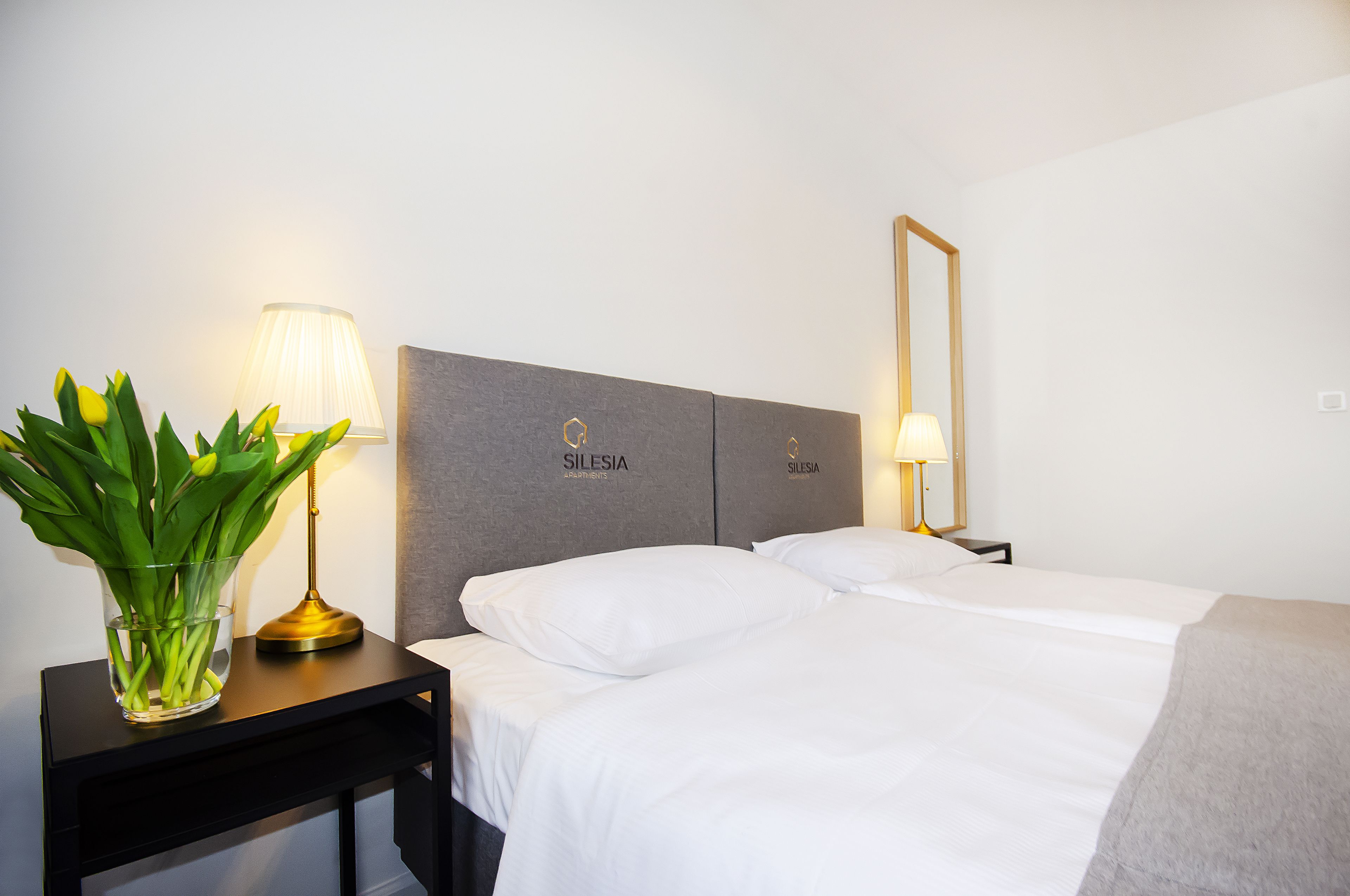 Una habitación de hotel con una cama, dos mesitas de noche, una lámpara y un espejo.