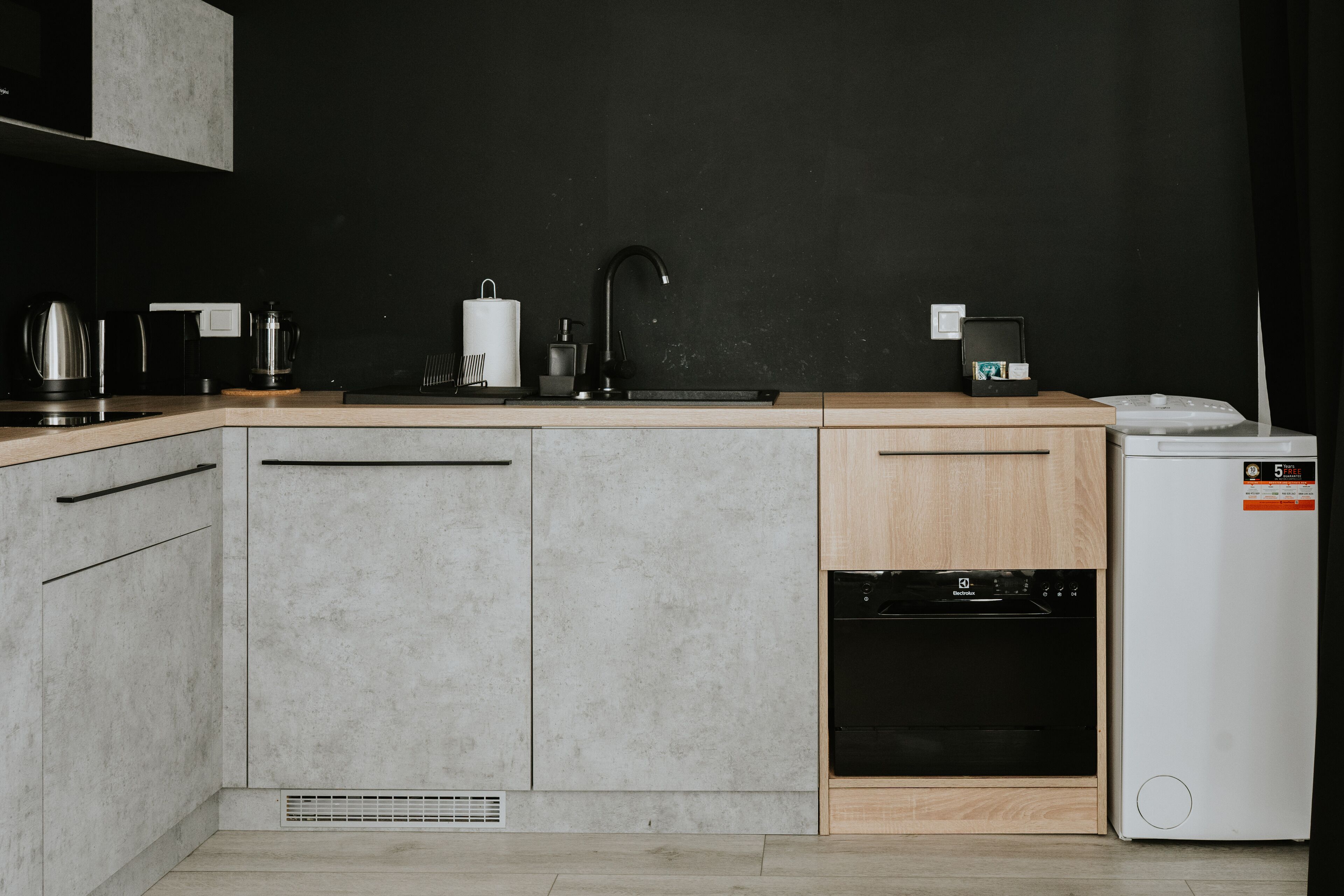 Una cocina moderna con encimera negra, armarios grises, un mueble de madera, horno empotrado y un refrigerador blanco.