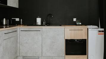 Una cocina moderna con encimera negra, armarios grises, un mueble de madera, horno empotrado y un refrigerador blanco.