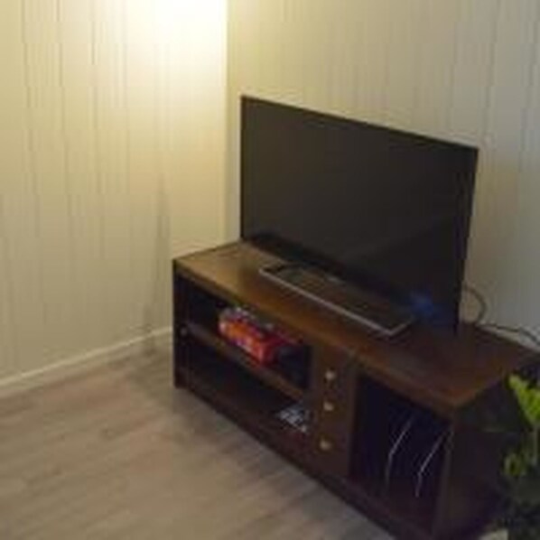 A small, dark wooden TV stand with a flat-screen TV, a shelf with a few items, and a power cord.