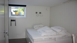 A bedroom with a bed, a window with potted plants, and a wall-mounted light fixture. - Solferie Apartment Arenfeldtsvei (Kristiansand)