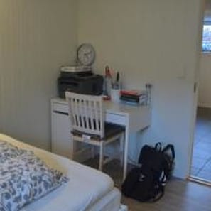 A bedroom with a bed, a desk with a chair, a clock, and a backpack on the floor.