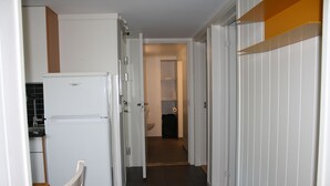 A narrow hallway with a refrigerator, a wooden chair, and a bathroom visible in the distance. - Solferie Apartment Arenfeldtsvei (Kristiansand)