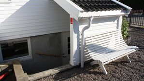 A white building with a sloped roof, a small entrance, and a bench outside. - Solferie Apartment Arenfeldtsvei (Kristiansand)