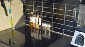 A kitchen with a black countertop, a blender, and a tiled backsplash. - Solferie Apartment Arenfeldtsvei (Kristiansand)