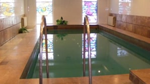 Une piscine intérieure avec des parois en verre transparent, un sol carrelé et des rampes en métal.