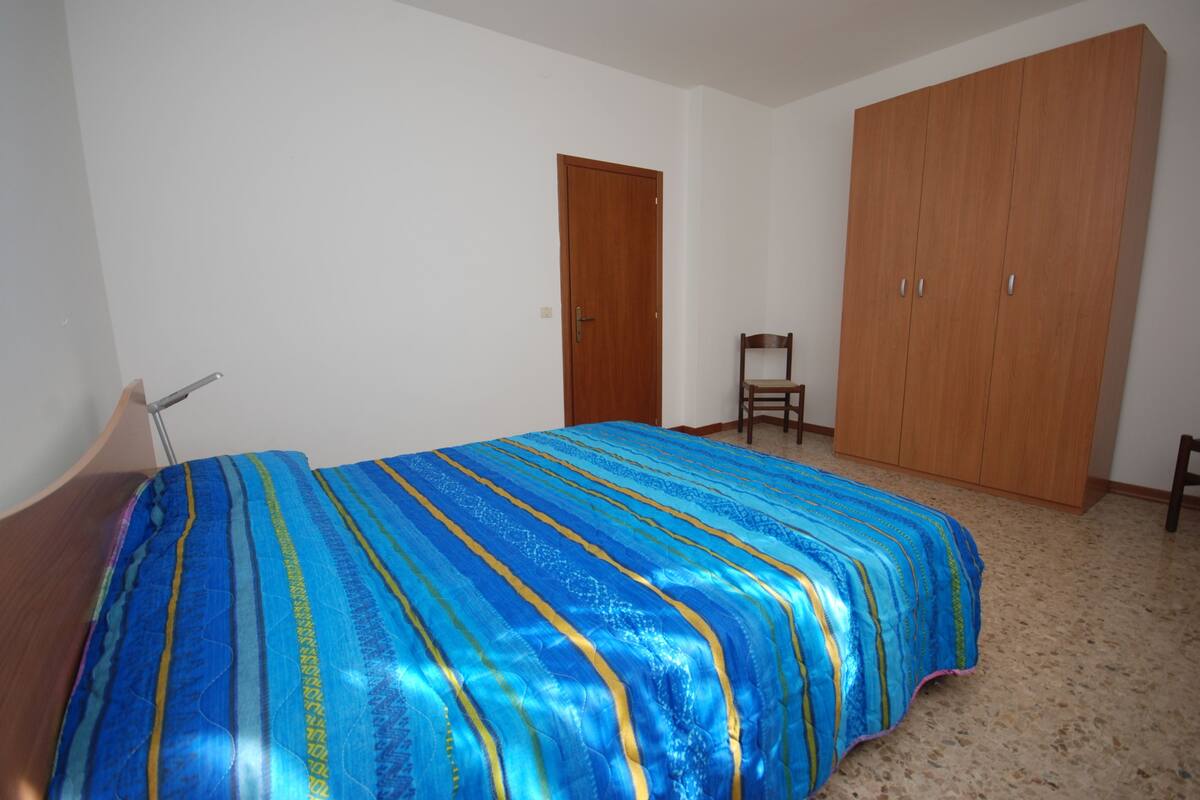 Um quarto com uma cama, um guarda-roupa de madeira e uma cadeira.