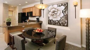 Un coin repas avec une table ronde, des chaises rembourrées, un panier de fruits et un tableau représentant des fleurs accroché au mur.