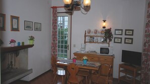 A dining area with a wooden table and chairs, a chandelier, a television, and a microwave. - Villa Schiller (Lignano Sabbiadoro)