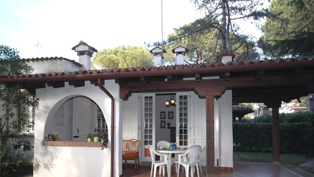 A patio with a white table and chairs, a covered seating area, and a window with plants. - Villa Schiller (Lignano Sabbiadoro)