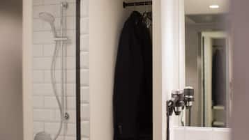 Un baño con ducha, una chaqueta negra colgada en un perchero y un espejo con toallero.