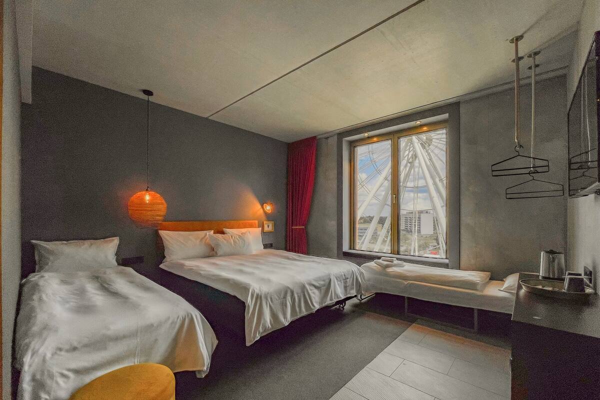 Habitación de hotel con dos camas, una ventana con vista a una noria, una pequeña zona de estar y una kitchenette.