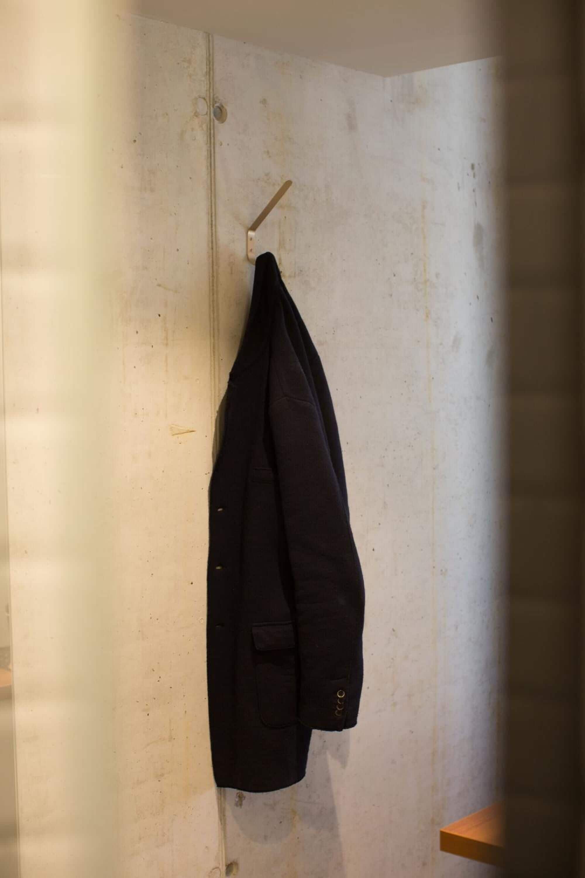 A room with a plain white wall, a wooden door, and a coat hanging on a hook.