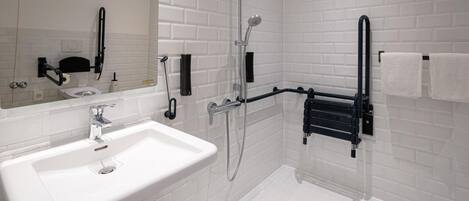 Un baño moderno con azulejos blancos tipo metro, un lavabo blanco, un espejo, un perchero negro y una ducha con cabezal de ducha de mano.
