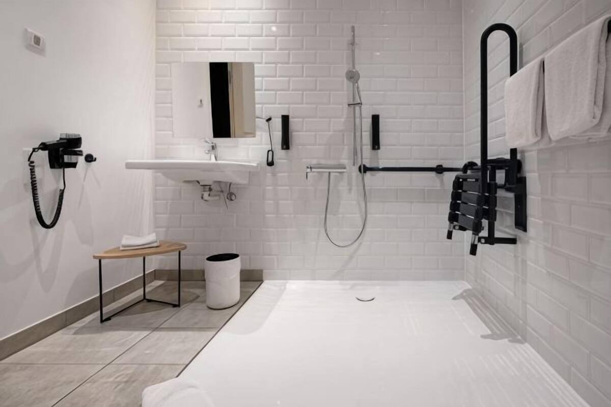 Un baño moderno con un lavamanos blanco, un espejo, un cabezal de ducha manual y un perchero para toallas.