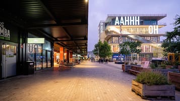 A modern urban plaza with a covered walkway, outdoor seating, and a prominent building with illuminated signage.