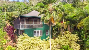 Une maison à deux étages, entourée d’une végétation tropicale luxuriante.