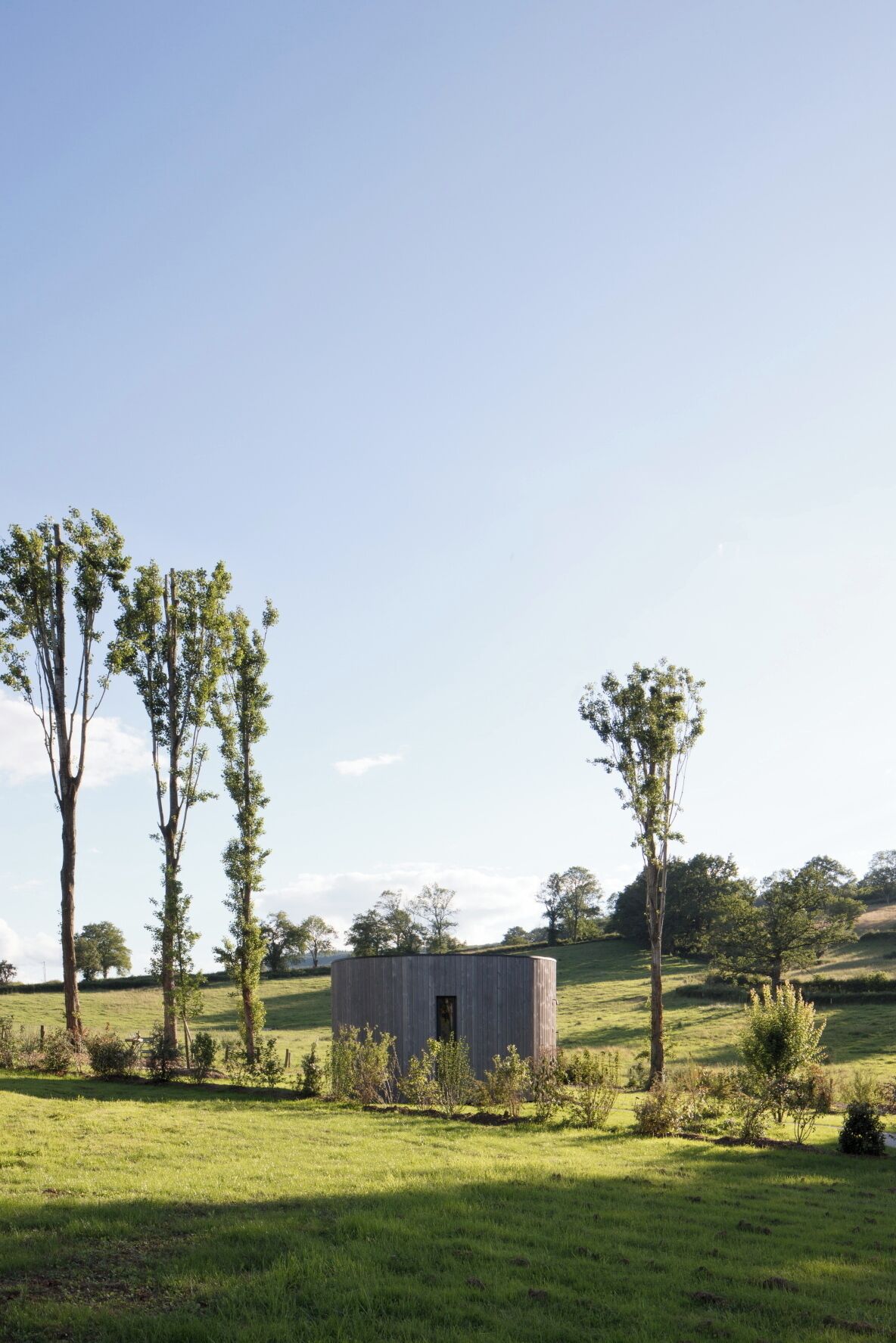 A small, rustic wooden cabin in a grassy field with trees around.