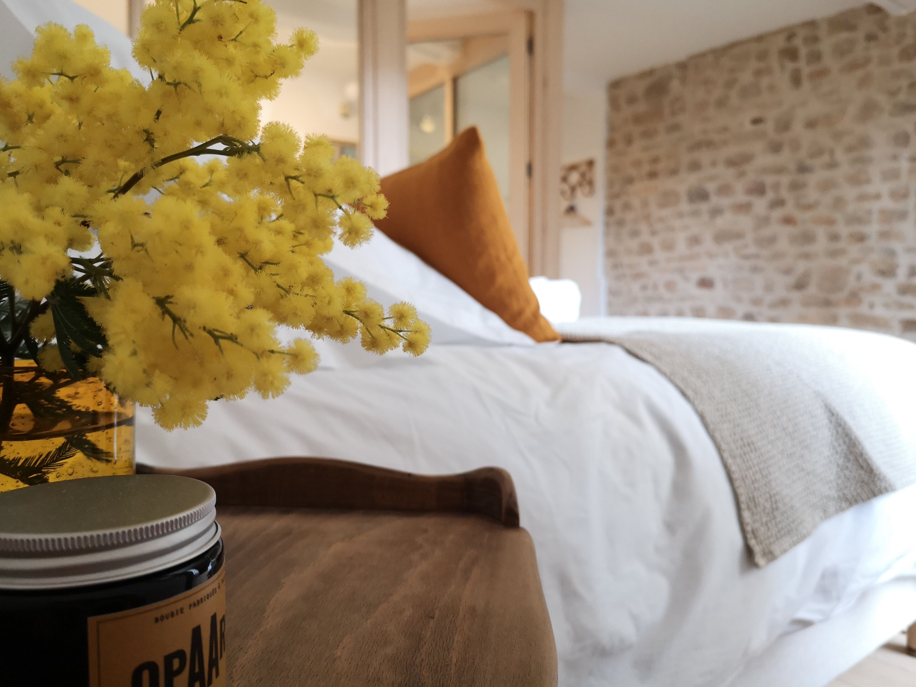 A bed with white bedding, a brown pillow, and a yellow flower arrangement on a bedside table.