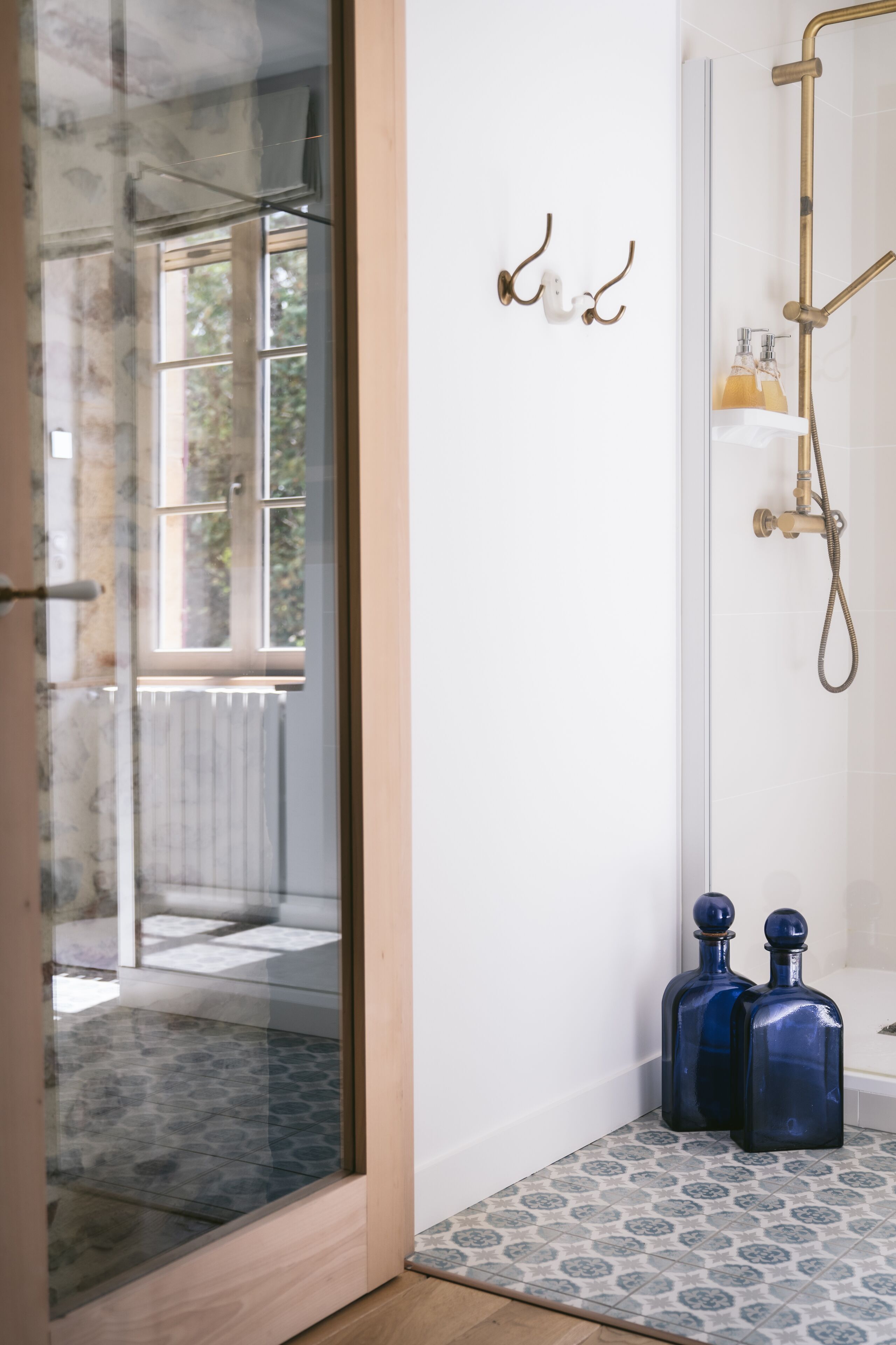 A modern bathroom with a glass door leading to a balcony, a shower with a gold faucet, and two blue bottles on the floor.