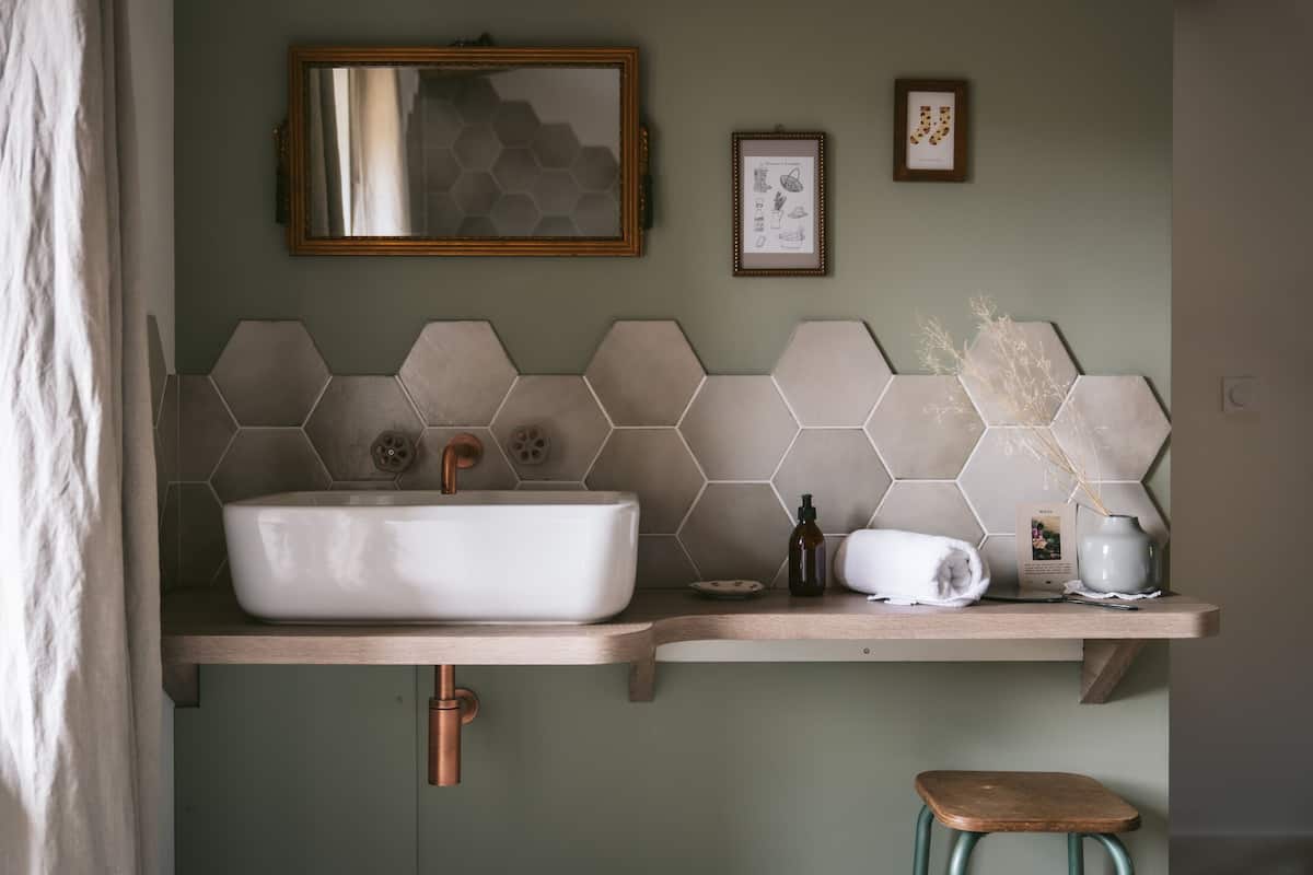 Ett badrum med ett vitt handfat, hexagonformade kakelplattor, en träpall och en handduk på bänkskivan.