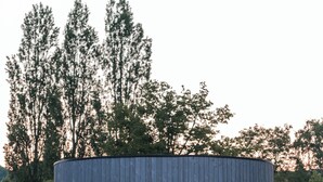 Eine moderne, einfache Blockhütte mit einer großen Schiebetür aus Glas, einem Bett und einer Pendelleuchte.