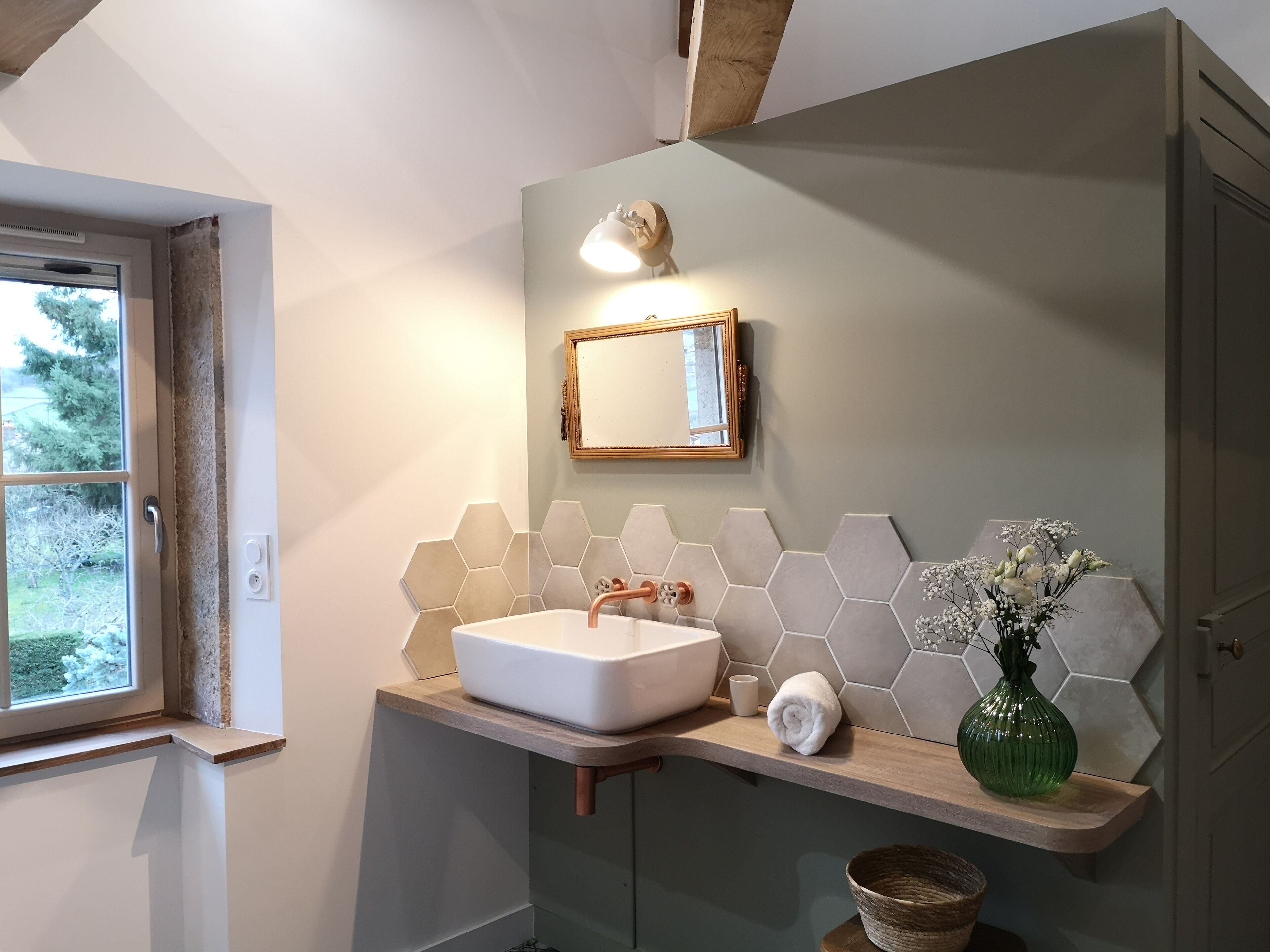 Ein Badezimmer mit Waschbecken, Holztischplatte, sechseckigen Fliesen, einem Spiegel und einer grünen Vase.