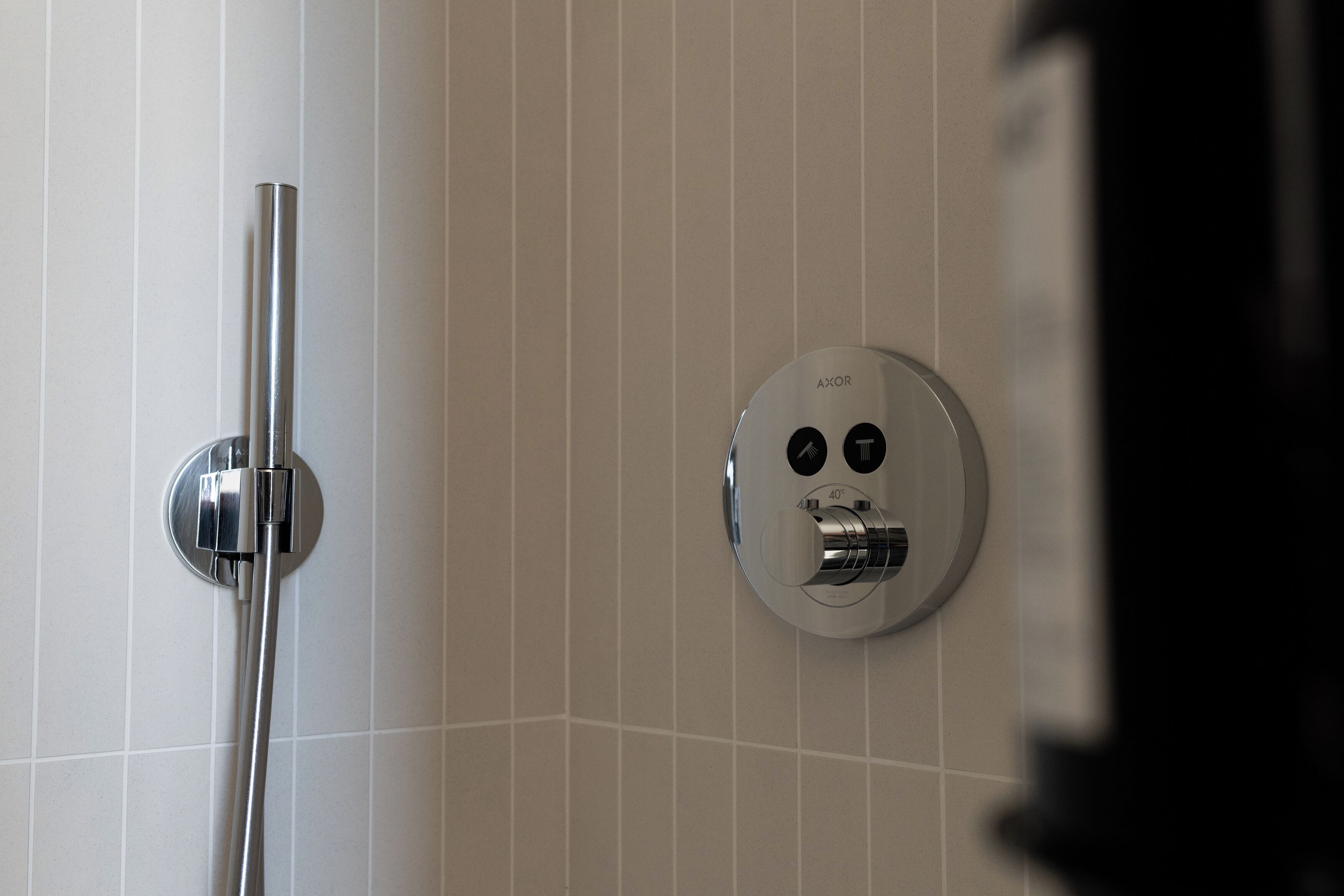 Une salle de bain moderne dotée d’un panneau de commande de douche fixé au mur et d’un pommeau de douche à main.
