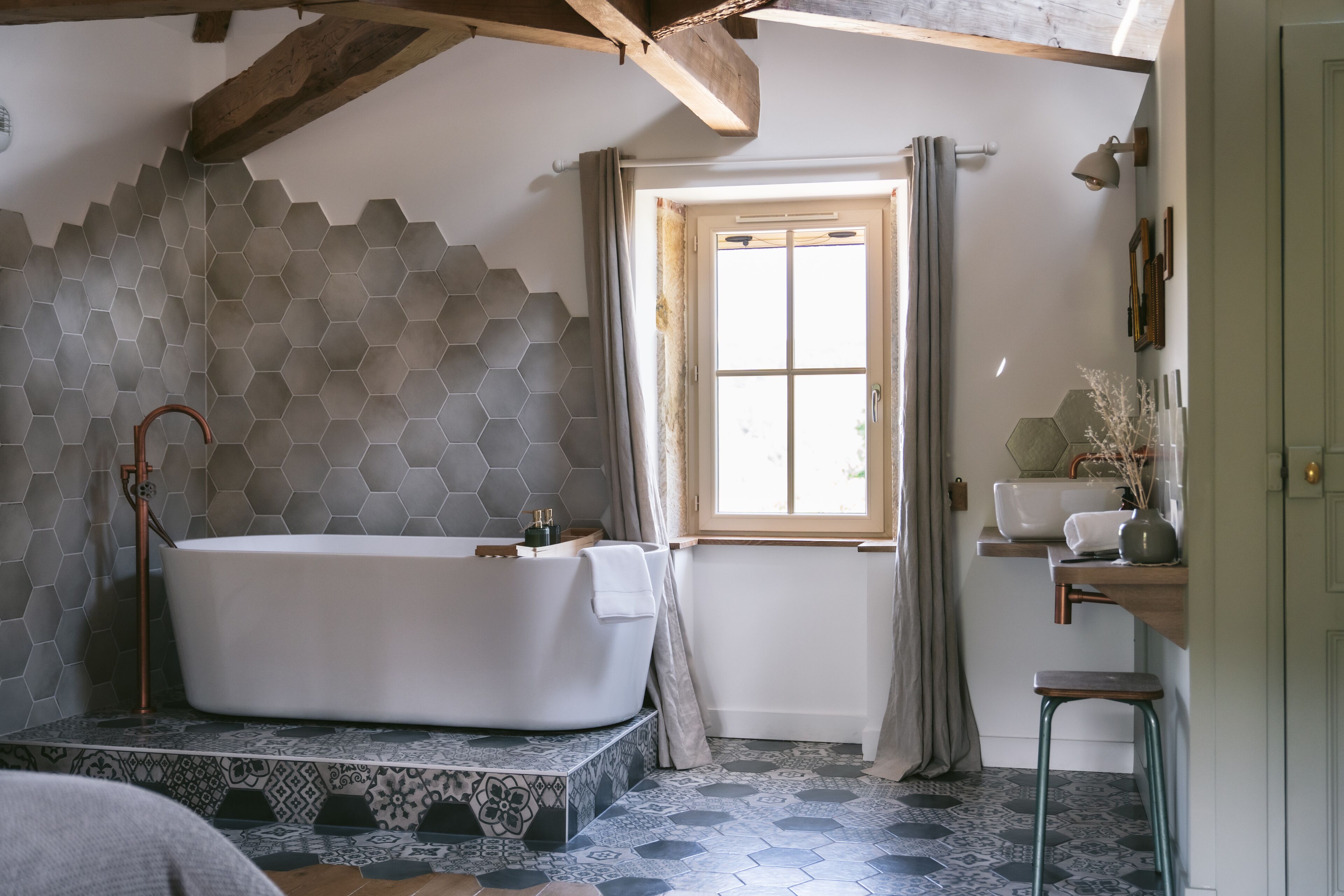 Une salle de bain moderne avec une baignoire sur pieds, une fenêtre avec des rideaux et un plafond en bois.