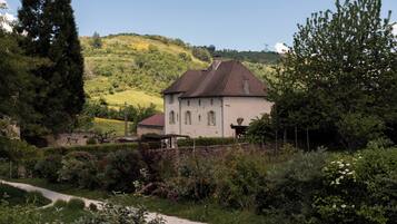 A house with a sloped roof, surrounded by lush greenery and a gravel path.