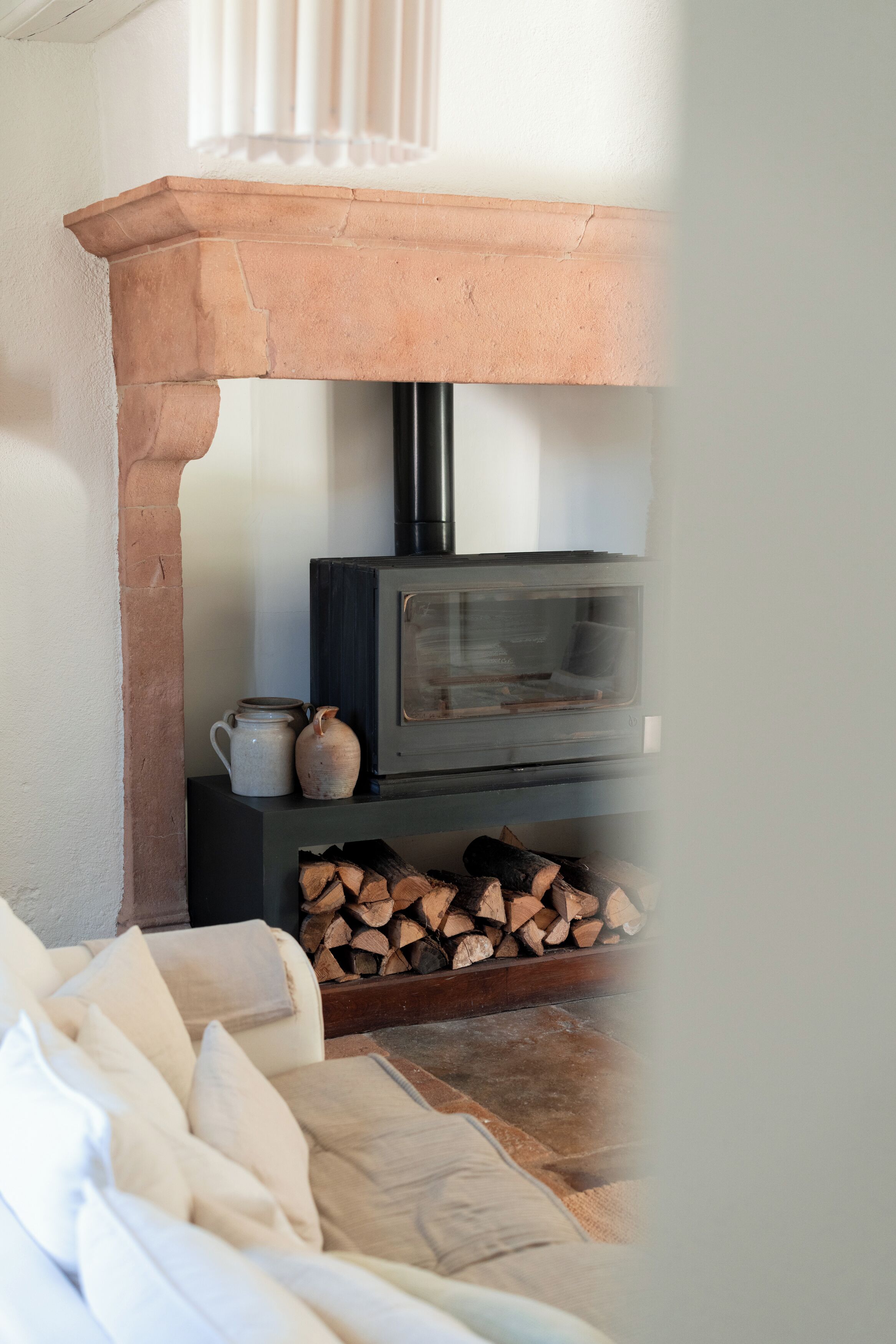 A fireplace with a stone mantel, a wood-burning stove, and a stack of firewood.