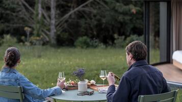 Two people dining outdoors at a table with a glass of wine, a vase with flowers, and a tray with food.